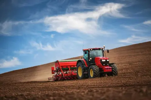 Czerwony traktor z siewnikiem orze pole. To obrazek z kategorii "prawo jazdy" kategorii T, pokazujący pracę w rolnictwie.