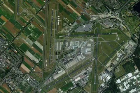 Widok z lotu ptaka na lotnisko Schiphol w Amsterdamie, otoczone polami i drogami.