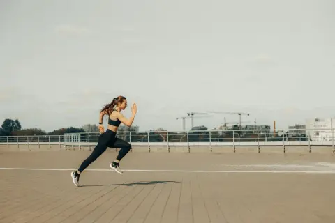 Kobieta w sportowym stroju biegnie, pokonując dystans 5 km. W tle widać miejską panoramę z dźwigami budowlanymi.