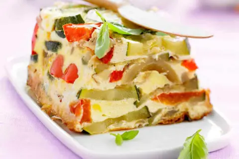 Tranche de terrine de légumes colorée, avec courgettes, poivrons rouges et une touche de basilic frais.