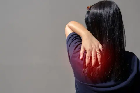 Douleur au muscle omoplate, une main masse la zone rouge sur le dos d'une femme.