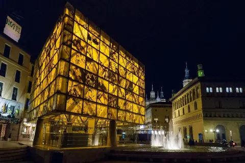 Edificio moderno y translúcido ilumina la noche junto a la fuente, cerca del museo del foro de Caesaraugusta.