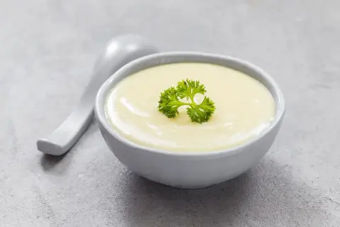 Kremowa zupa, idealna na dietę bezresztkową, ozdobiona listkiem pietruszki. Obok leży łyżka.