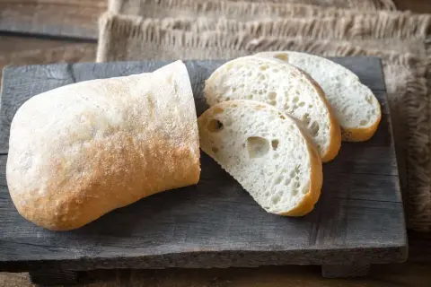 Ein rustikales ciabatta mit sauerteig, aufgeschnitten auf einem Holzbrett.