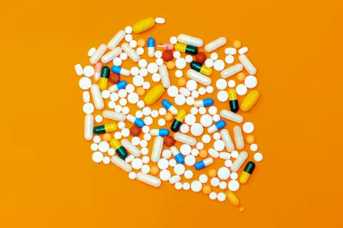 Rozsypane tabletki i kapsułki, w tym leki opioidowe, na pomarańczowym tle.