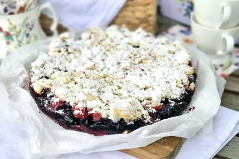 Pyszne ciasto kruche z owocami leśnymi, posypane cukrem pudrem i kruszonką. Idealne na letnie popołudnie.