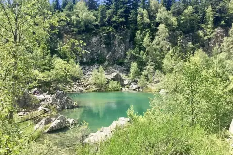 Un paisible lac bleu en Haute-Loire, entouré de rochers et d'une forêt verdoyante.