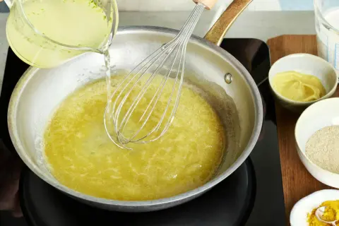 Flüssigkeit wird in eine Pfanne mit einem Schneebesen gegossen, um eine cremige vegane Hollandaise zuzubereiten.