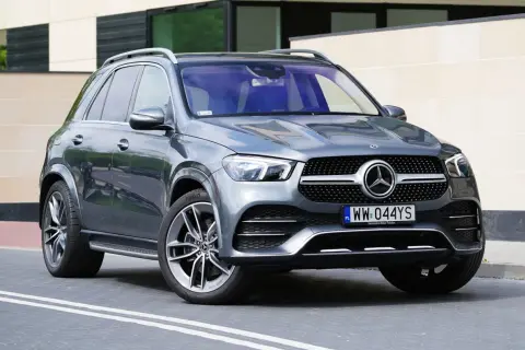 Szary Mercedes GLE 300 d stoi przed nowoczesnym budynkiem. Elegancki SUV z charakterystycznym grillem i felgami.