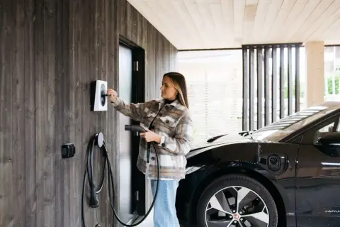 Kvinna laddar elbil vid laddbox. Frågan "hur lång tid tar det att ladda en elbil 22kw" är relevant här.