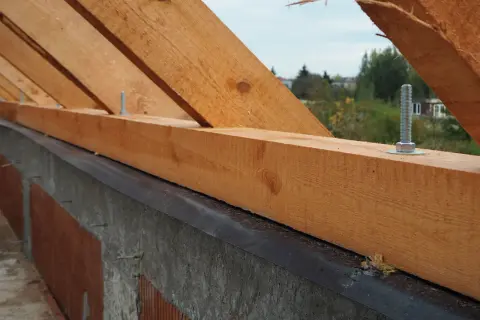 Drewniana murłata przykręcona do betonu śrubami, bez wieńca. Konstrukcja dachu w budowie.
