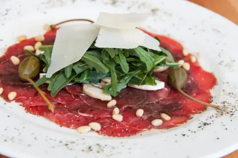 Delicato carpaccio di manzo con rucola, scaglie di parmigiano, pinoli, capperi e funghi champignon.