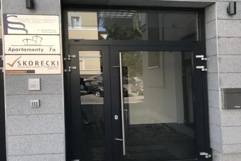 Drzwi wejściowe do budynku z tabliczkami: "Apartamenty 7a" i "SKORECKI Kancelaria Doradcy Finansowego".