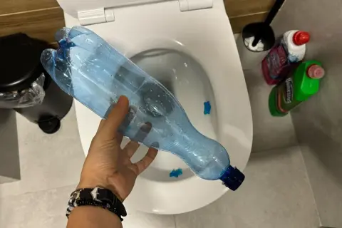 Ręka trzyma plastikową butelkę nad toaletą, pokazując, jak odetkać toaletę bez przepychaczki.