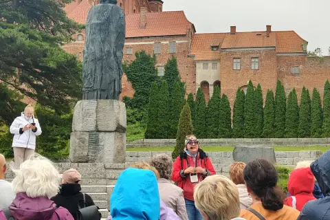 Wycieczka po Fromborku: przewodnik opowiada o Koperniku przy pomniku, w tle katedra. Atrakcje Fromborka odkrywane przez turystów.