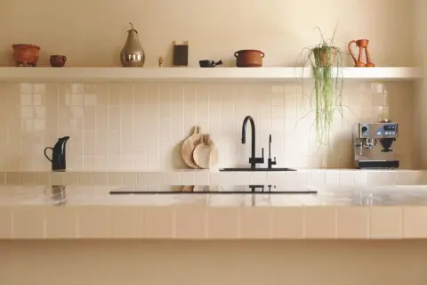 Encantadora cocina con azulejos claros, grifo negro y cafetera. Las últimas tendencias en azulejos para cocinas se reflejan en este diseño minimalista y funcional.
