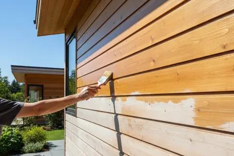 Application d'un lazur bois sur une façade en bois. La moitié est traitée, l'autre attend son tour.
