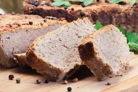 Pokrojony pasztet mieszany drobiowo-wieprzowy, przyprawiony ziarnami pieprzu, na desce.