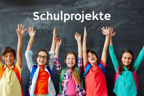 Fünf fröhliche Grundschüler mit Rucksäcken und erhobenen Armen vor einer Tafel, die "Schulprojekte" anzeigt.