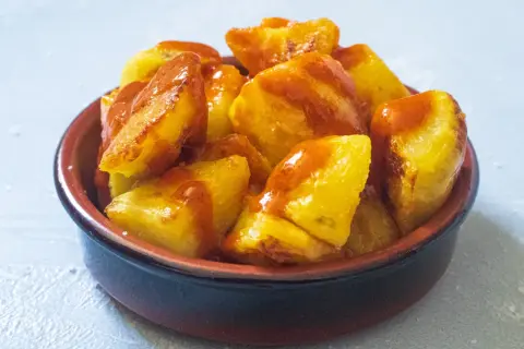 Knusprige Kartoffelstücke, überzogen mit einer würzigen Sauce, serviert als köstliche Patatas Bravas in einer rustikalen Schale.