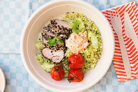 En skål med tillagad quinoa, skivat kött med sesamfrön, hummus, gurka och körsbärstomater. Perfekt för en snabb och hälsosam lunch.
