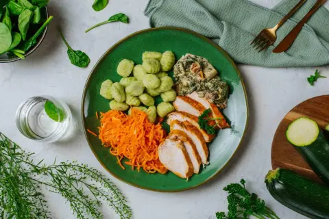 Zielony talerz z kurczakiem, zielonymi kluseczkami, startą marchewką i kremowym szpinakiem. Idealne dieta ketogeniczna - przepisy dla początkujących za darmo.