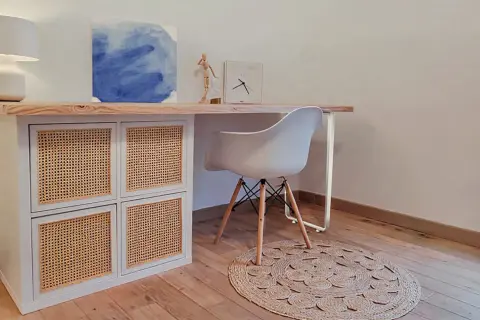 Bureau en pin relooké avec des portes en rotin. Une chaise blanche et un tapis rond complètent ce coin bureau moderne.