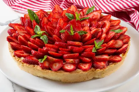 Deliziosa crostata alla crema, ricoperta da fragole fresche affettate e guarnita con foglie di menta.