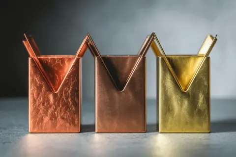 Trois porte-stylos aux formes géométriques, en laiton et cuivre, aux textures variées.