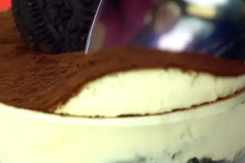 Une cuillère plonge dans un délicieux tiramisu Oreo, saupoudré de cacao. Un dessert gourmand à savourer !