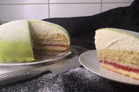 En vacker prinsesstårta med grön marsipan och ett lager sylt. En bit är upplagd på en tallrik.