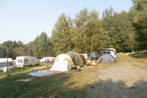 Na kempingu Złoty Potok rozstawione namioty i przyczepy kempingowe wśród drzew.