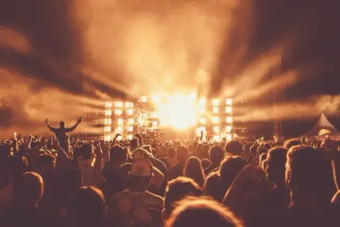 Tłum ludzi na Sunrise Festival Poland, z rękami w górze, w blasku świateł scenicznych i dymu.