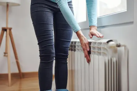 Mani che toccano un termosifone freddo, preoccupazione perché i termosifoni non si scaldano e la casa è gelida.