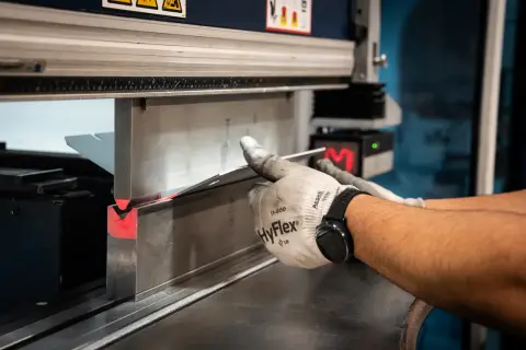 Operator w rękawicach formuje metal na prasie krawędziowej. Różne rodzaje prasy pozwalają na precyzyjne gięcie.