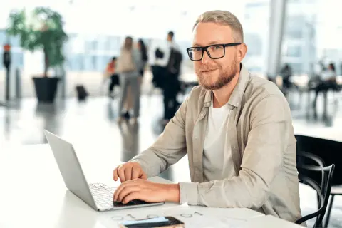 Mężczyzna w okularach, z brodą, pracuje na laptopie. Jego kod zawodu to informatyk, który tworzy cyfrowe rozwiązania.