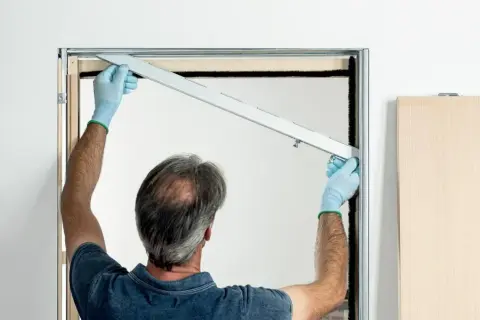 Installazione controtelaio porta scorrevole in cartongesso. L'operaio con guanti azzurri posiziona la guida superiore.