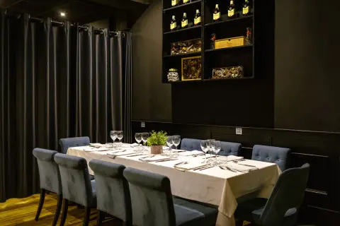 Mesa elegante con sillas azules y mantel blanco, lista para el menú del día de la buganvilla. Botellas de vino en estantería.