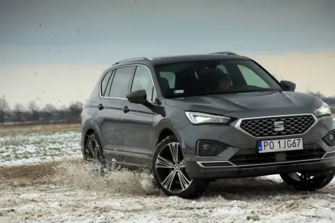 Szary Seat Tarraco SUV przemierza błotniste, zaśnieżone pole, wzbijając chmury brudu.