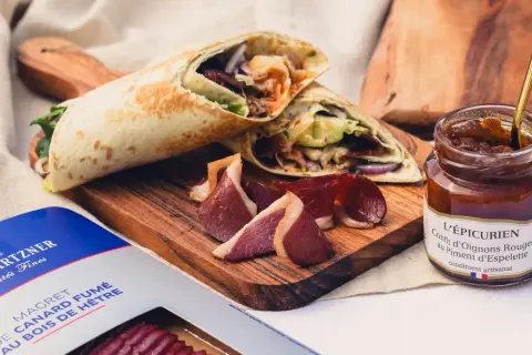 Wrap de magret de canard fumé, servi avec des tranches de canard et un confit d'oignons rouges.