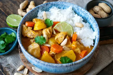Ein köstlicher Massaman Curry mit Hühnchen, Kartoffeln, Karotten und Erdnüssen, serviert mit Reis und Limettenspalten.