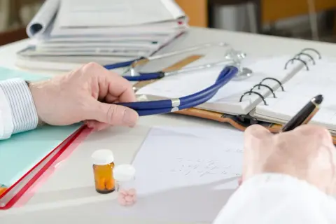 Lekarz pisze receptę, obok stetoskop i leki. Czy do dermatologa na NFZ trzeba mieć skierowanie?