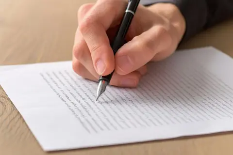 Dłoń pisze piórem na papierze. To może być wzór listu motywacyjnego, który pomoże Ci w karierze.