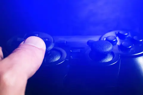 Dłoń naciska joystick kontrolera do gier w niebieskim świetle.