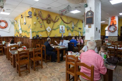 Gente comiendo en la abacería el arrecife, decorada con motivos marineros. Mesas de madera y paredes amarillas con redes y barcos.