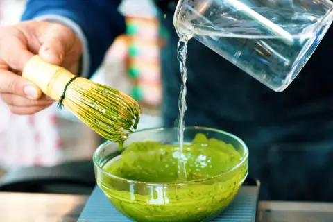 Préparation d'un matcha apaisant pour l'intestin irritable. Un fouet en bambou est utilisé pour mélanger la poudre verte dans un bol.