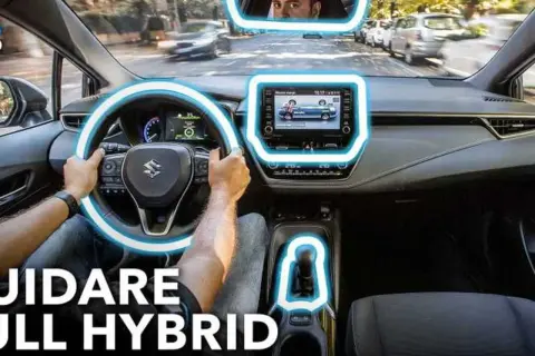 Interno di un'auto ibrida, con le mani sul volante e il display centrale acceso. Scopri il significato di auto ibrida e guida in modo ecologico.
