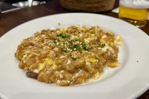 Delicioso revuelto de bacalao con trocitos de frutos secos y perejil picado, servido en un plato blanco.