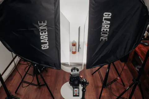 Profesjonalna fotografia produktowa jak zacząć? Zestaw oświetleniowy z dwiema lampami Glareone, aparatem i butelką w tle.