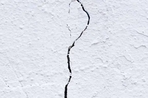 Una pared blanca con textura rugosa muestra grietas por dilatación, una línea oscura que se abre paso a través de la superficie.